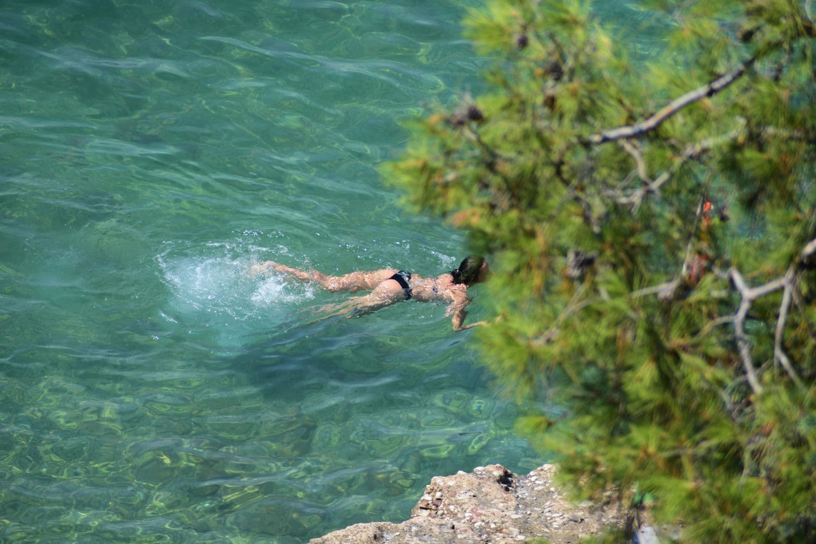 Άτομο κολυμπά σε καθαρά θαλάσσια νερά, συμβολίζοντας την αναζήτηση ανακούφισης από τον καύσωνα και τις επιπτώσεις του στα θαλάσσια οικοσυστήματα.