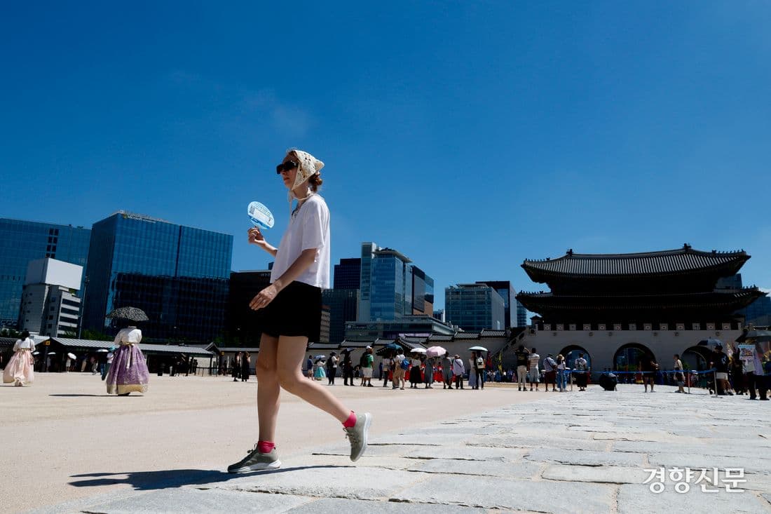 도심 광장에서 부채로 더위를 식히며 걷는 사람