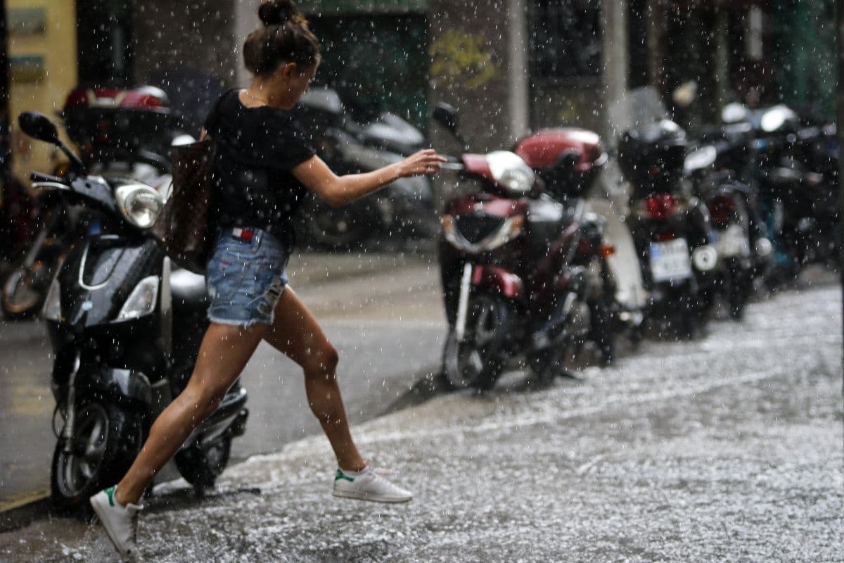 Άνθρωπος τρέχει μέσα σε δυνατή βροχή και χαλάζι στην Ελλάδα, απεικονίζοντας τις ακραίες καιρικές αλλαγές.