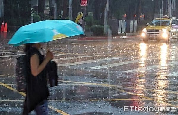 台灣城市街道上，行人撐傘在大雨中行走，反映台灣持續面臨的洪水警報。