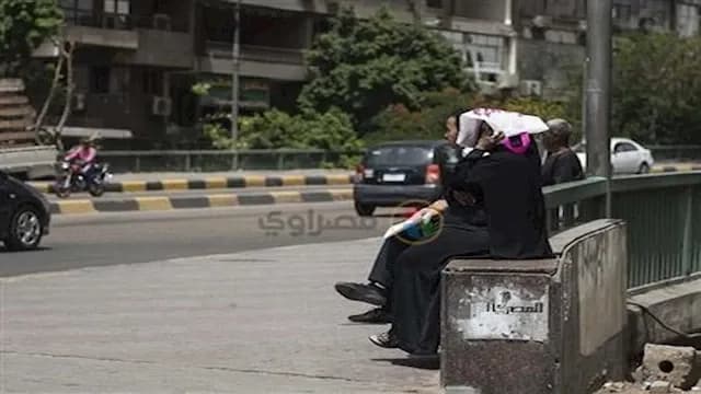 أشخاص يجلسون على مقعد في شارع بالقاهرة أو الدلتا، يتأثرون بالحرارة الشديدة والرطوبة العالية التي تجعل المهام اليومية صعبة.