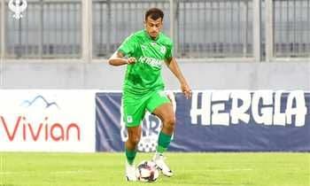 لاعب كرة قدم بقميص أخضر يراوغ بالكرة في الملعب.