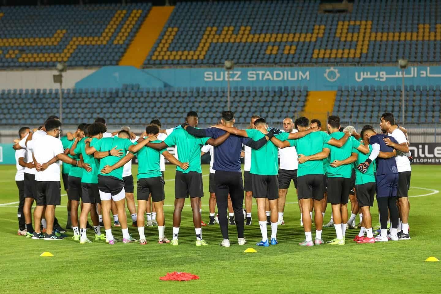 لاعبو النادي المصري يتجمعون في حلقة على أرض الملعب، يظهرون روح الفريق والتماسك.