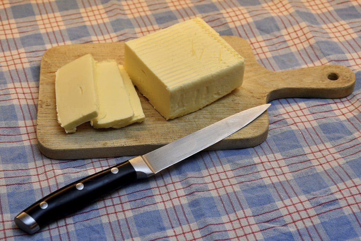 A block of butter on a wooden cutting board with a knife.