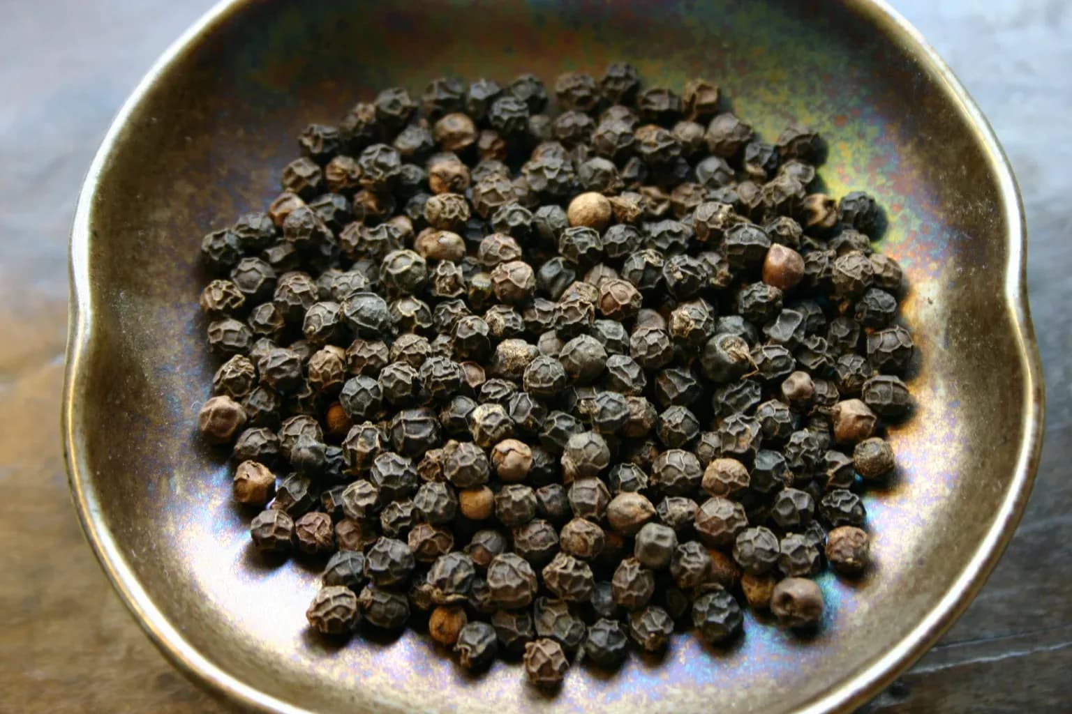 A bowl filled with dried black pepper corns, representing the global commodity trade of pepper.