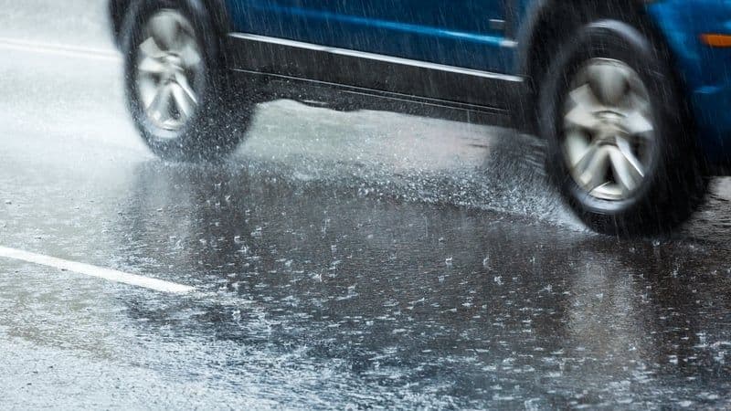A car drives through heavy rain on a wet road, illustrating difficult travel conditions during a yellow weather warning in Ireland.