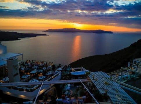 A dramatic sunset over a Greek island, with clouds reflecting the sky's changing colors, representing sudden weather shifts.