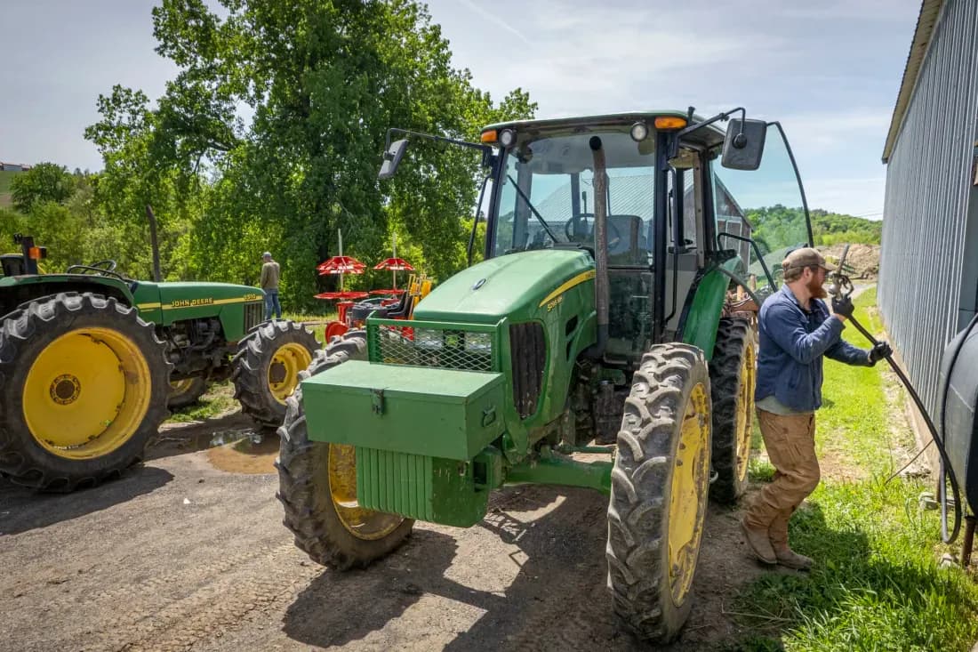 A farmer fueling a tractor on a farm, representing the operational costs associated with agricultural production.