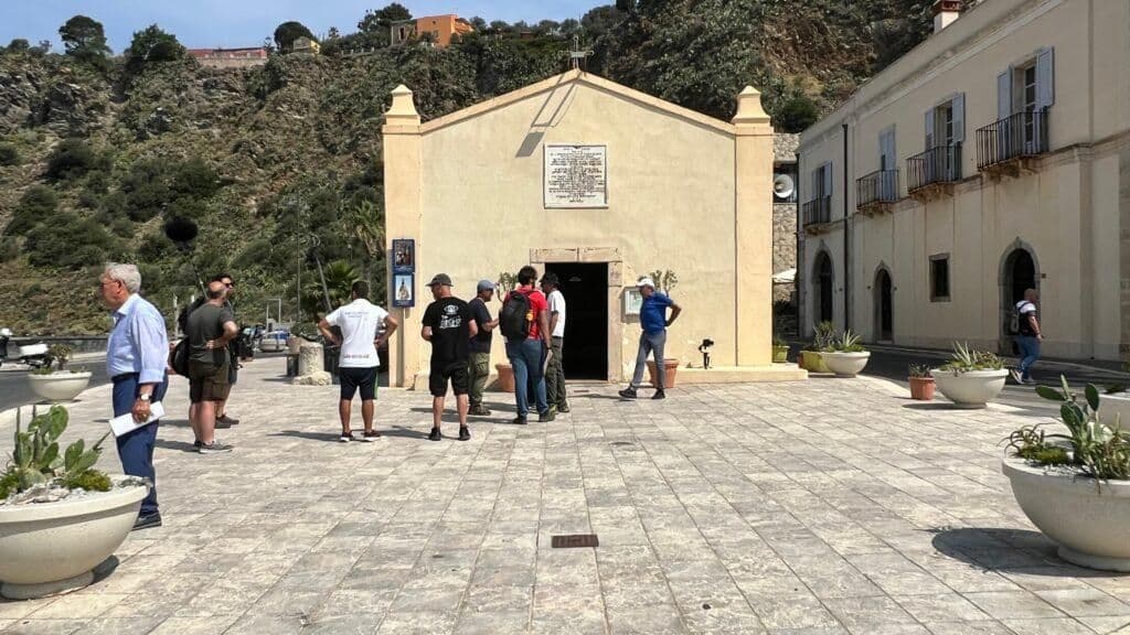 A film crew gathers outside a charming church in a Milazzo town square, reflecting the strong community, art, and faith of the hinterland.