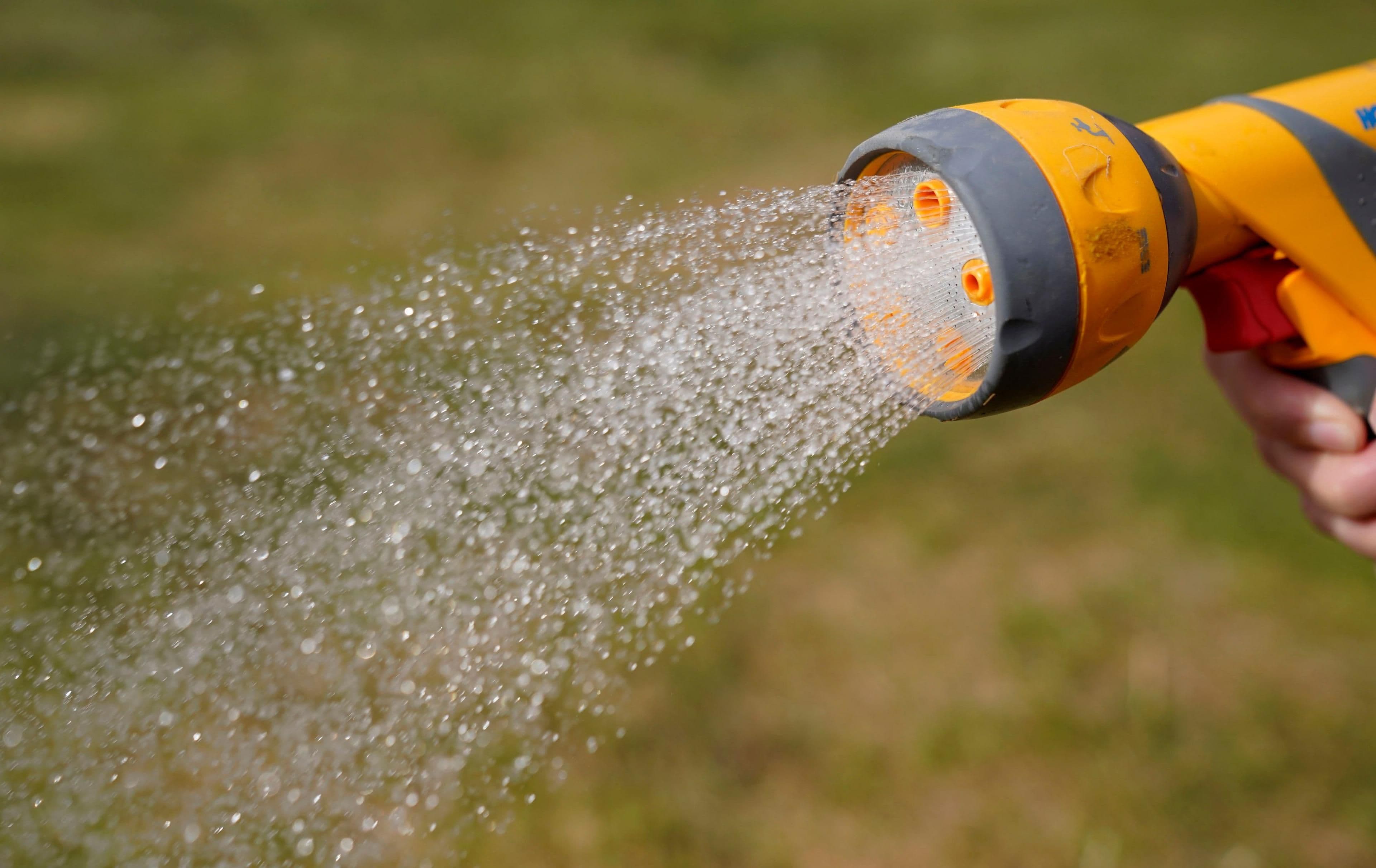 A hand holding a garden hose with water dripping, symbolizing hosepipe bans and water scarcity during drought.