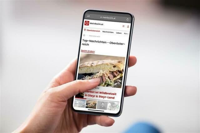 A hand holding a smartphone displaying a news website, representing consumers accessing information and reporting food safety concerns.