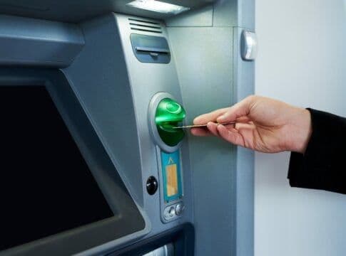 A hand inserting a digital card into an ATM, representing the use of the Thessaly-Evros Pass.