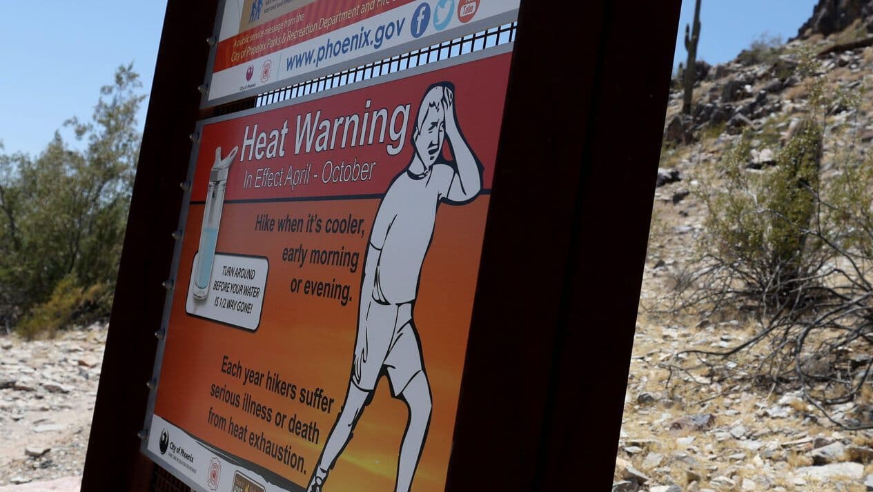 A 'Heat Warning' sign at a Phoenix trailhead, advising hikers about the dangers of extreme temperatures and heat exhaustion.