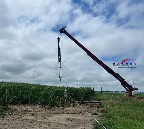 A large crane from Dawson Public Power repairing a power line in a cornfield under a cloudy sky, illustrating the impact of severe weather in the Midwest.