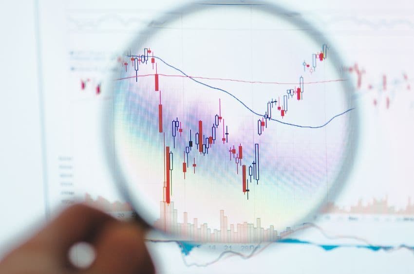 A magnifying glass examining a stock market candlestick chart, symbolizing financial analysis and market scrutiny of IHI's stock performance.