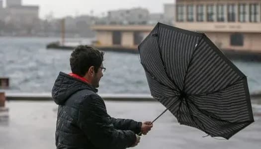 A man struggling to hold onto his umbrella against strong winds and rain, illustrating the warnings for associated atmospheric phenomena like strong winds.