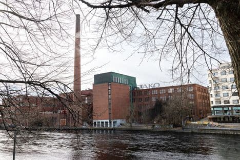 A Metsä Board mill with a tall chimney next to a river, representing a past mill closure contrasted with Metsä Group's current strategy.