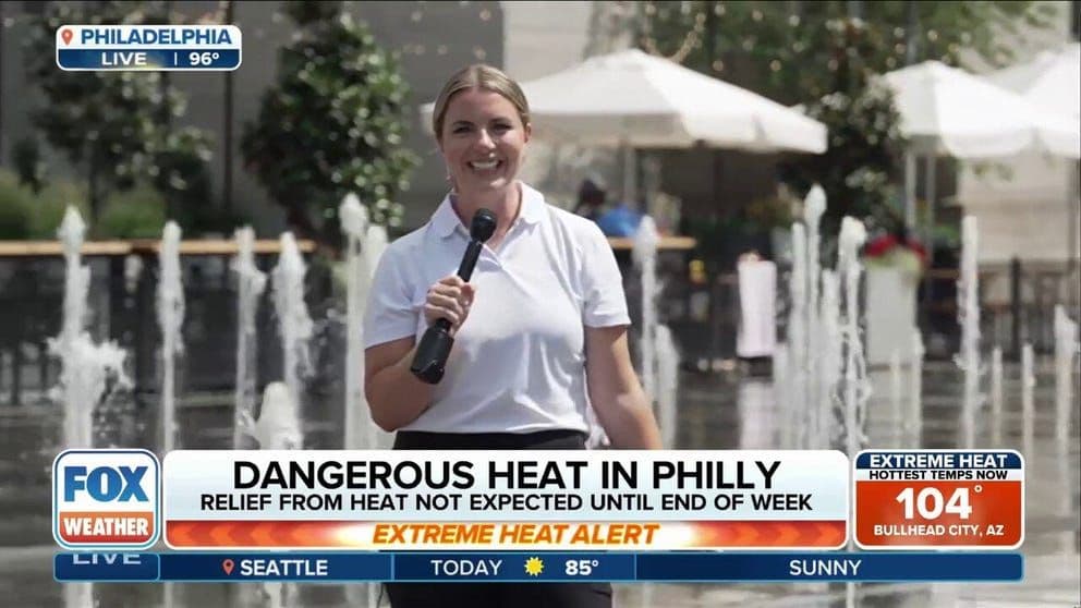 A news reporter standing in front of a splash pad in Philadelphia, discussing the extreme heat.