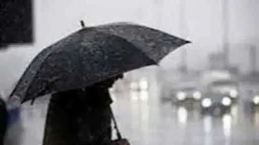A person holding an umbrella in the rain, representing the potential for thunderstorms and atmospheric instability.