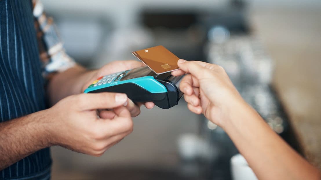 A person paying with a credit card on a POS terminal, illustrating digital financial transactions.