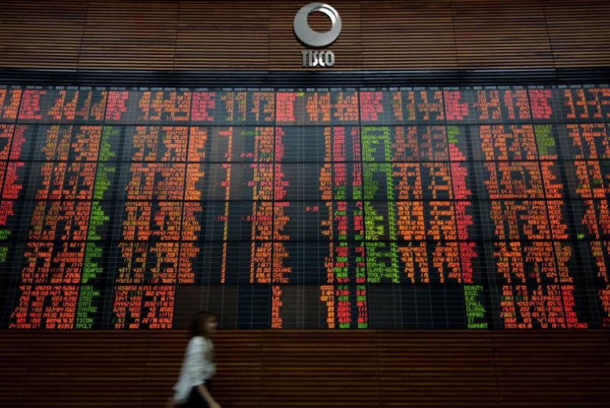 A person walking past a large electronic market display board showing financial data.
