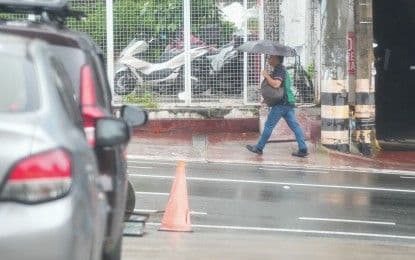 A person walking with an umbrella on a rainy street, illustrating the impact of the habagat monsoon in the Philippines.