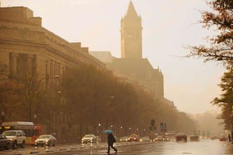 A person with an umbrella crosses a busy, rain-slicked street in Washington D.C. during a heavy downpour, highlighting urban rainfall.
