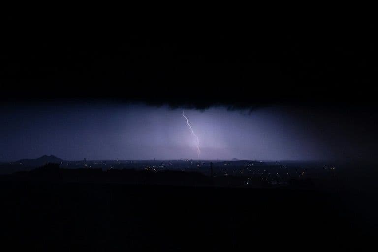 A powerful lightning bolt illuminates a dark, stormy sky over a distant city, symbolizing severe weather and hailstorms.