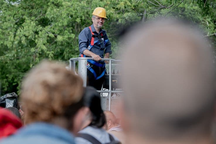 A protester in a hard hat standing on a hydraulic lift, looking over the walls of the Hatvanpuszta estate during the transparency protest.