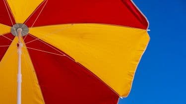 A red and yellow beach umbrella against a clear blue sky, symbolizing the global challenge of extreme heat and climate change.