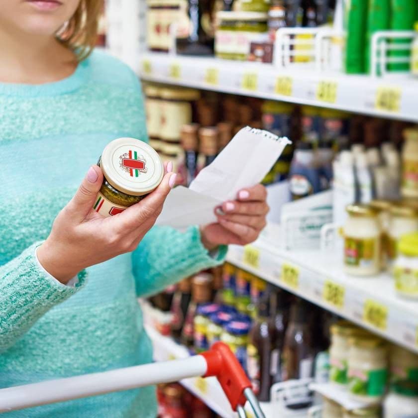 A shopper in a supermarket aisle examining a private label product and a receipt, highlighting quality control and consumer vigilance.
