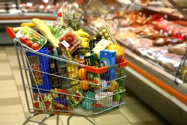 A shopping cart filled with various grocery staples at a supermarket.