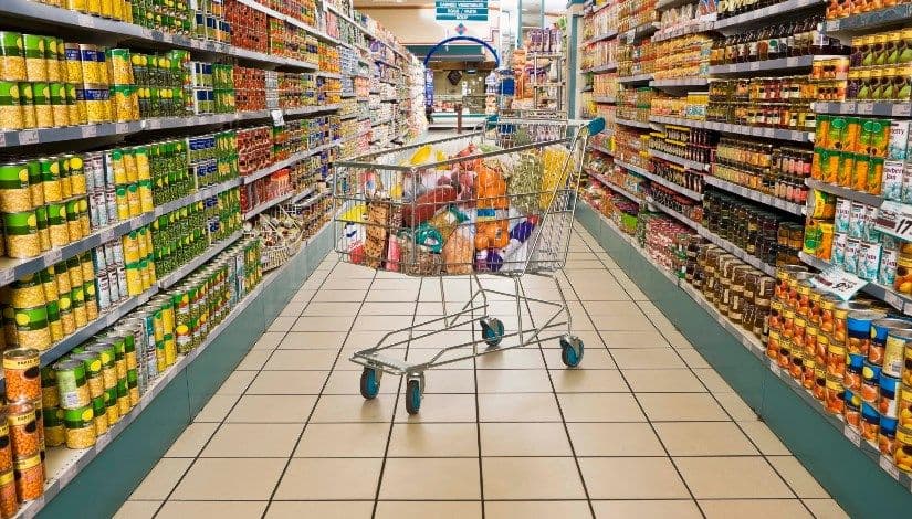 A shopping cart in an aisle of a grocery store, representing the potential impact of supply chain disruptions on food retail prices.