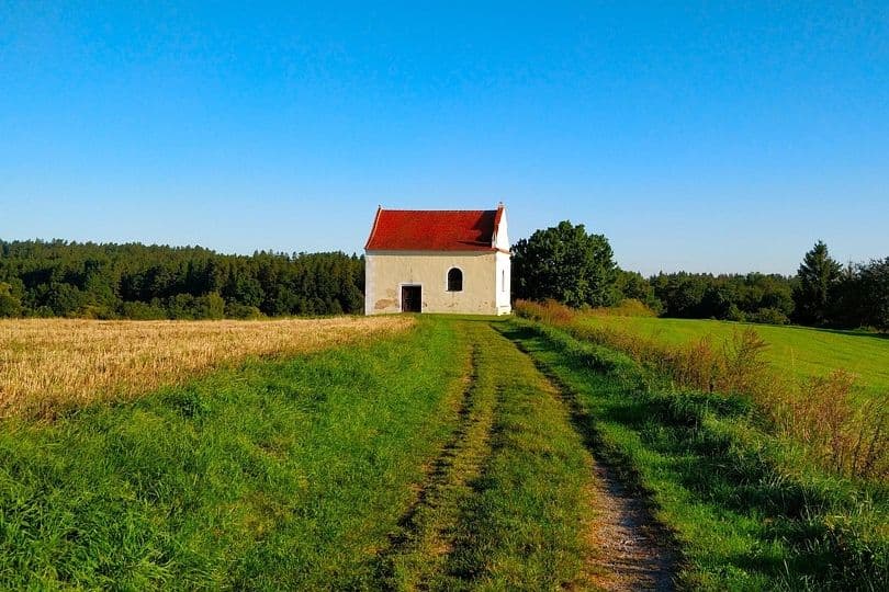 A small chapel in a green field under a clear blue sky, illustrating Hungary's settled, sun-drenched August weather.