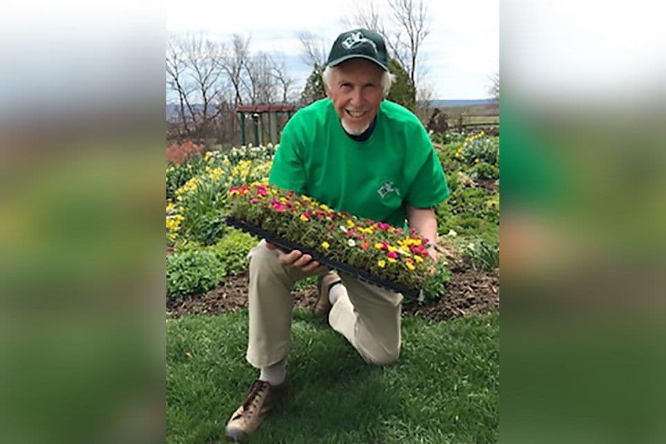 A smiling gardener holding a tray of colorful young plants, ready for August planting to ensure future blooms.