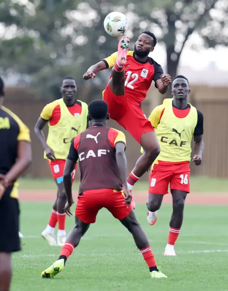 A Ugandan football player in red and black uniform performing an overhead kick during a match.