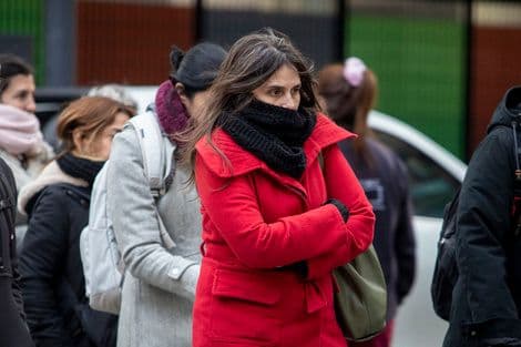 A woman bundled in a red coat and black scarf, looking cold, representing Argentina's sharp winter return.
