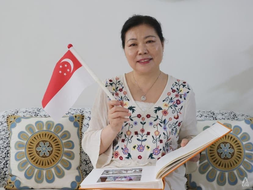 A woman proudly holding a Singapore flag while looking at a photo album, representing personal growth and national pride in Singapore's journey of ascent.