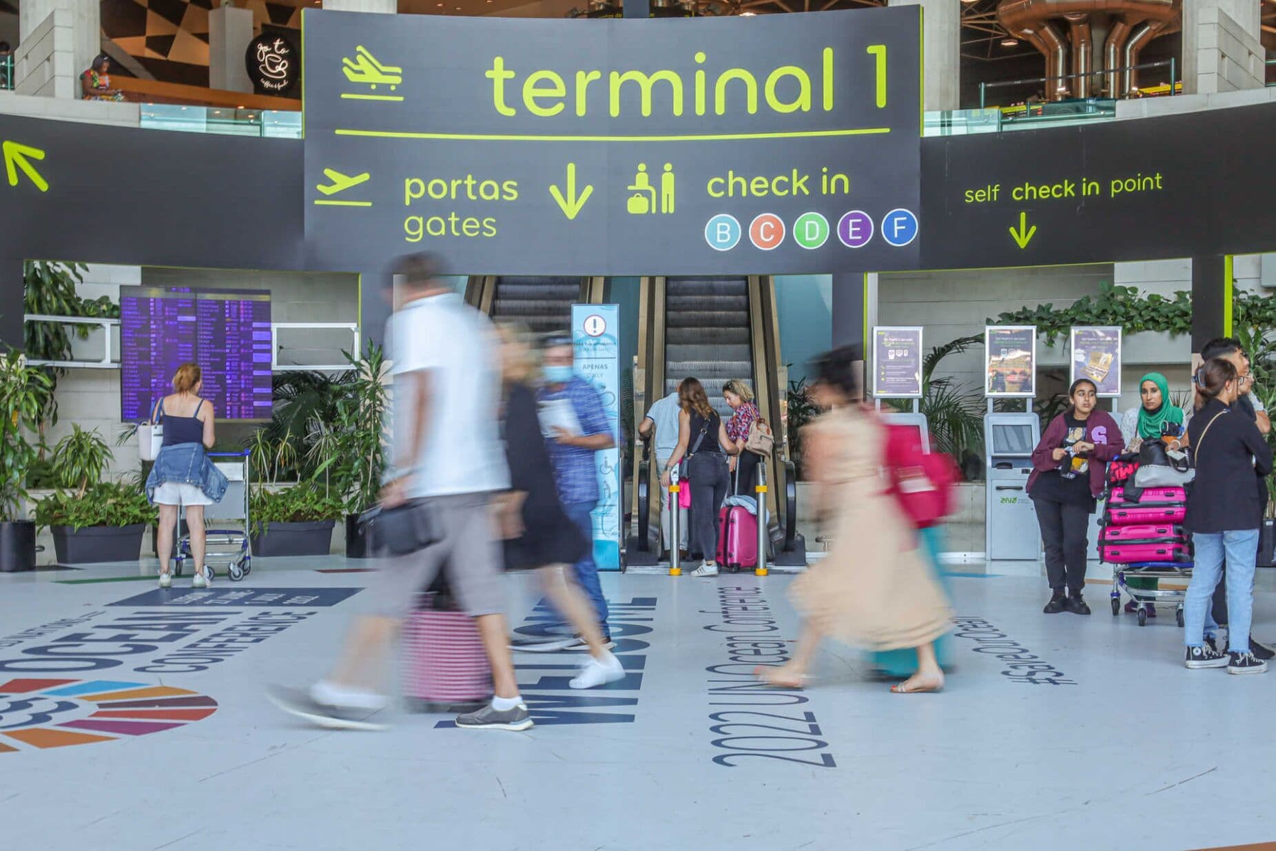 Aeroporto de Lisboa com passageiros e sinalização de terminal, simbolizando o acordo entre o SIMA e Menzies que cancela as greves.