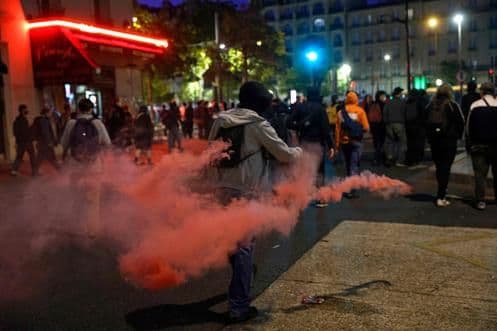 Affrontements entre manifestants et forces de l'ordre avec un jet de grenade lacrymogène, illustrant la rhétorique du 'chaos' et la réponse sécuritaire de l'État.