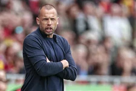 Ajax manager John Heitinga with a serious expression and crossed arms on the sideline.