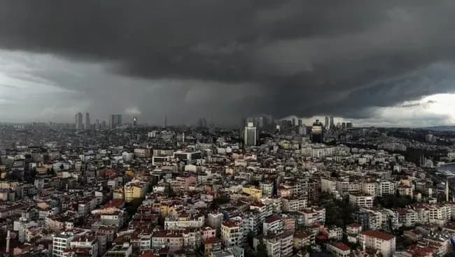 An aerial view of a sprawling Turkish city, likely Istanbul, under a dramatic dark, cloudy sky, signifying the arrival of heavy rain and a significant weather change.