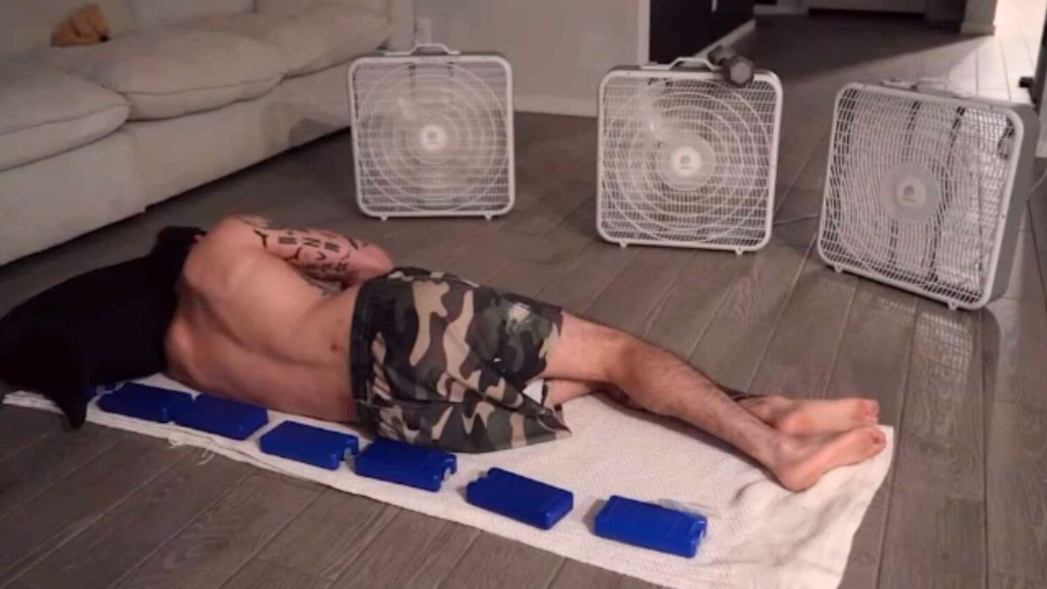 An Arizona man lying on the floor with ice packs and fans, demonstrating personal adaptation to extreme heat without air conditioning.