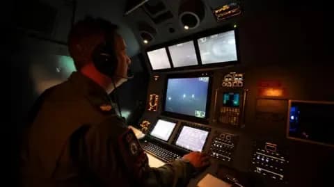 An RAF Mission System Operator wearing a headset, intently monitoring multiple screens in a dimly lit cockpit, showcasing human-machine collaboration in air operations.
