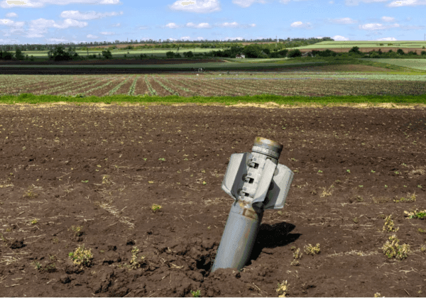 An unexploded bomb or missile partially buried in a Ukrainian agricultural field, illustrating the constant threat of shelling and landmines to farmers.