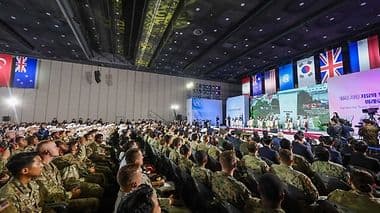 Audience internationale avec des drapeaux nationaux, symbolisant la coopération et la stabilité économique mondiale.