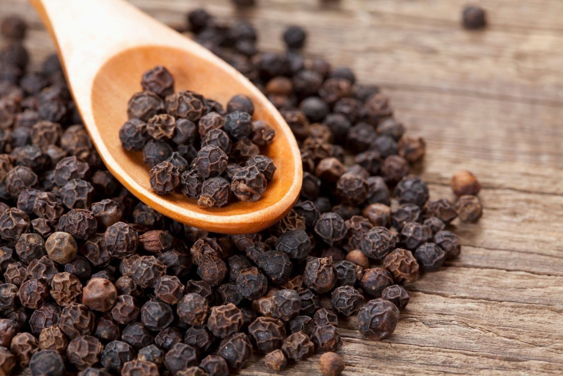 Black peppercorns in a wooden spoon, illustrating the global spice commodity market.