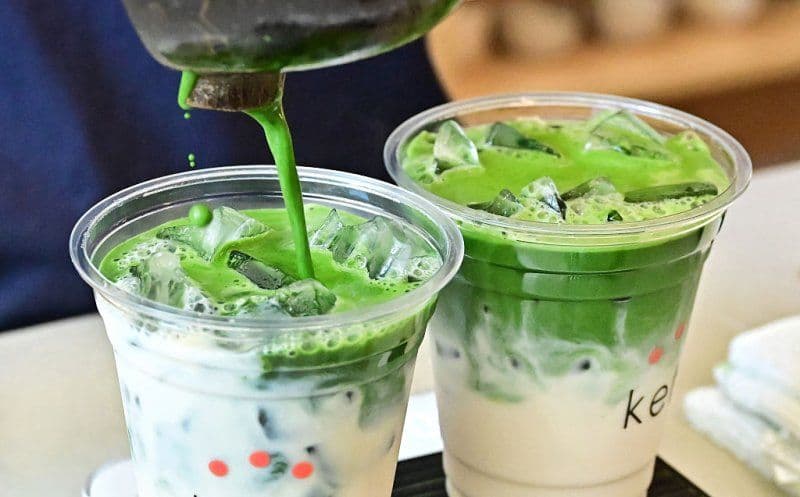 Bright green matcha being poured into a cup with ice and milk, creating a layered matcha latte, symbolizing its global popularity.