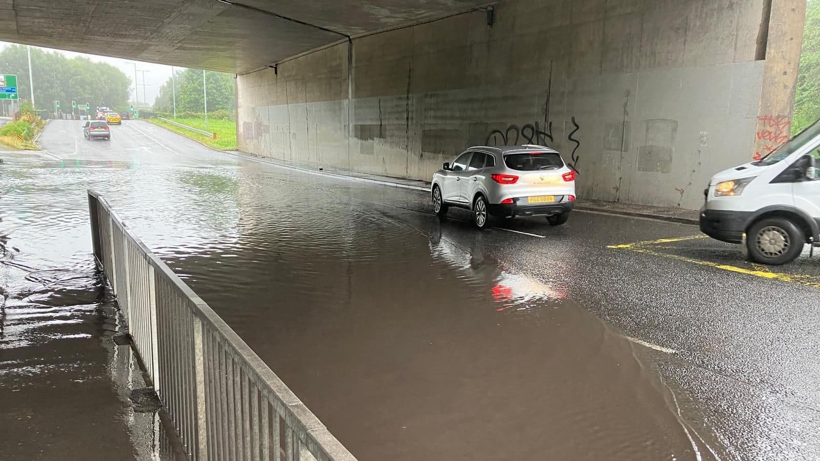 Cars driving through a flooded underpass in the UK, illustrating recent heavy summer rainfall.