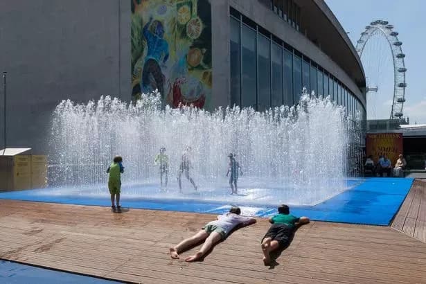 Children playing in a public fountain near the London Eye, illustrating how people cope with UK summer heatwaves.